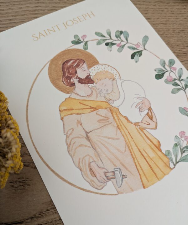 Affiche A5 d'une illustration peinte à la main représentant saint Joseph artisan tenant l'enfant Jésus dans ses bras, entourée d'une couronne florale.
