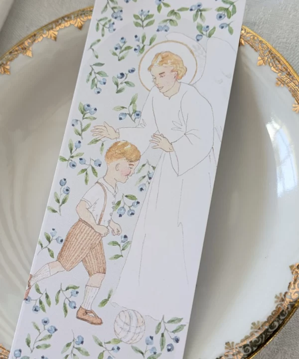Signet marque-page représentant un ange gardien veillant sur un petit garçon qui joue au ballon, entourés de feuillage et de baies violettes. Avec sa courte prière à l'ange gardien, c'est idéal en cadeau de naissance, de baptême ou pour marquer les pages d'un livre.